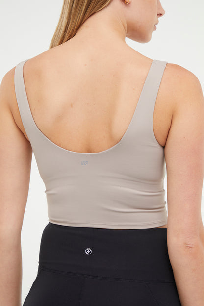 Close up back view of woman wearing a beige sports bra and black leggings on a white background. 