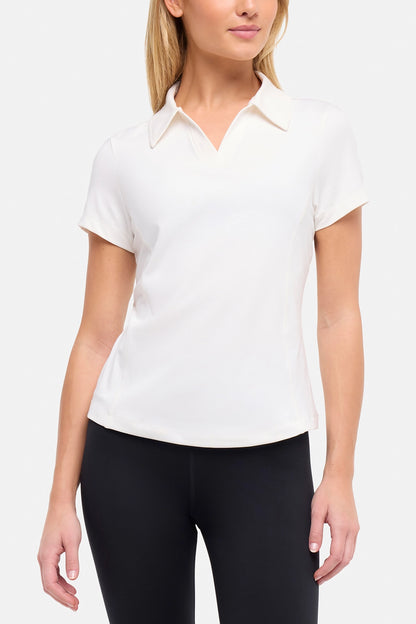 Front view of woman wearing a white short-sleeve polo shirt and black pants on a plain background. 
