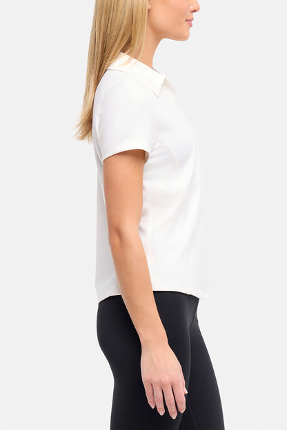 Side view of woman wearing a white short-sleeve polo shirt and black pants on a plain background. 