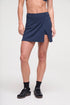 Front view of woman wearing a navy blue tennis skirt and black sneakers on a light gray background. 