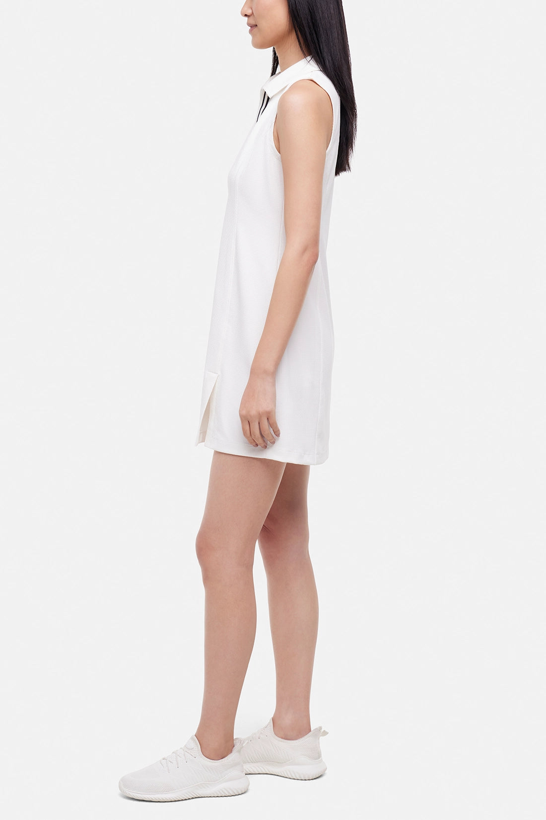 Side view of woman wearing a white sleeveless polo dress with a black stripe collar on a white background. 