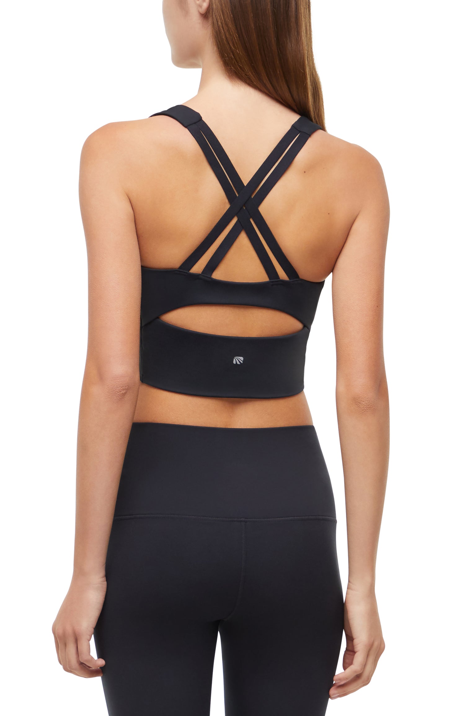 Back view of woman wearing a black sports bra with criss-cross back design and black leggings on a white background. 