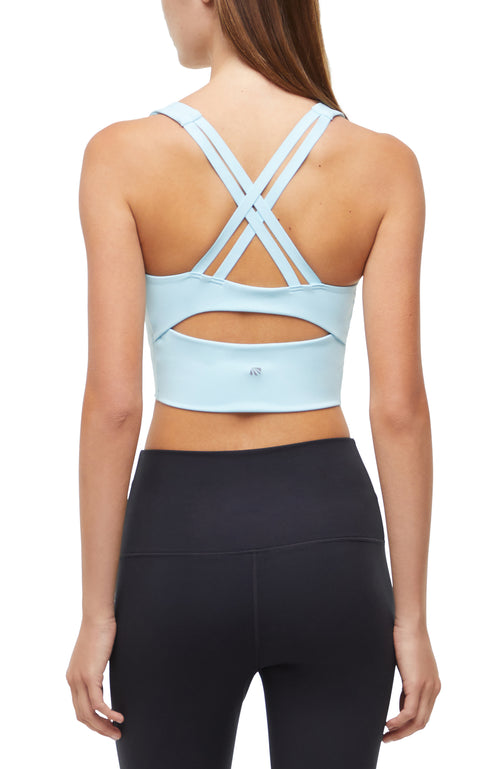 Back view of woman wearing a light blue sports bra with criss-cross back design and black leggings on a white background. #color_ocean-current