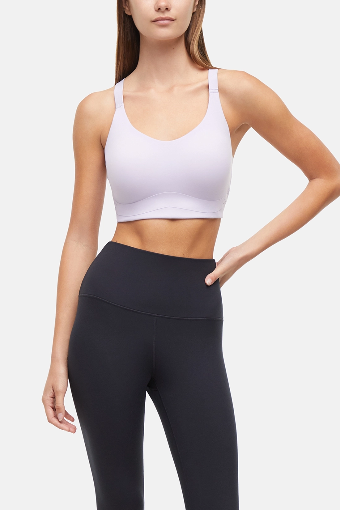 Front view of woman wearing a lilac sports bra and black leggings on a light gray background. 