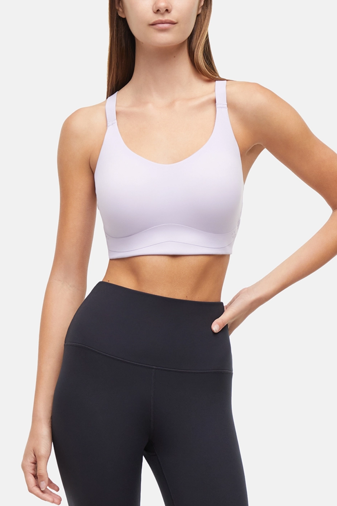 Front view of woman wearing a lilac sports bra and black leggings on a light gray background. 