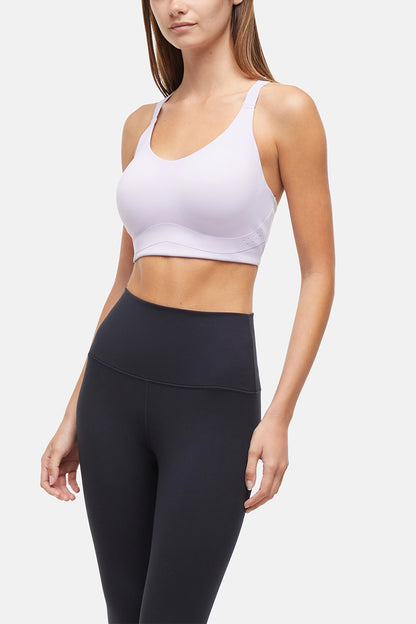 Front view of woman wearing a lilac sports bra and black leggings on a light gray background. 