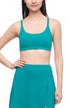 Front view of woman wearing a teal green sports bra and skirt on a light gray background. 