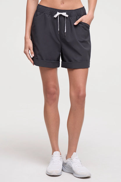 Front view of woman wearing dark gray shorts with a white drawstring, standing on a white background. 