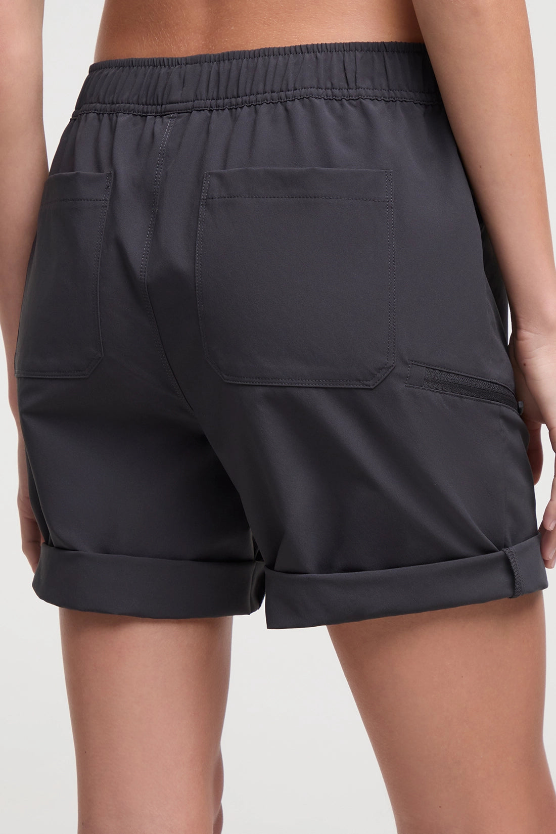 Back view of woman wearing dark gray shorts standing on a white background. 