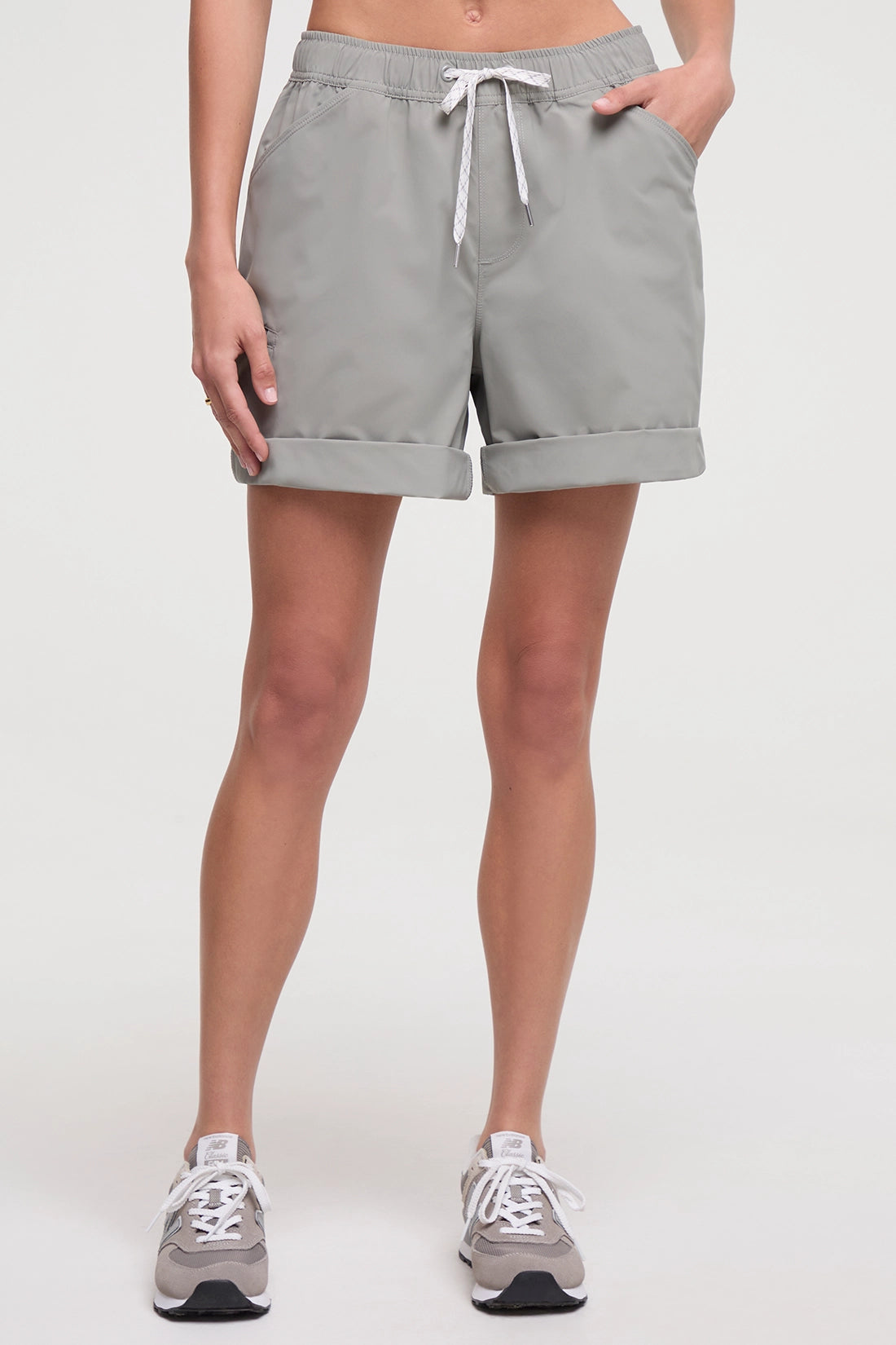 Front view of woman wearing taupe gray shorts with a white drawstring, standing on a white background. 