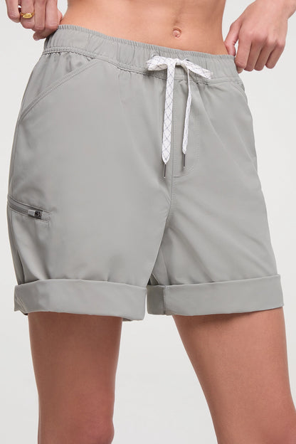 Front view of woman wearing taupe gray shorts with a white drawstring, standing on a white background. 