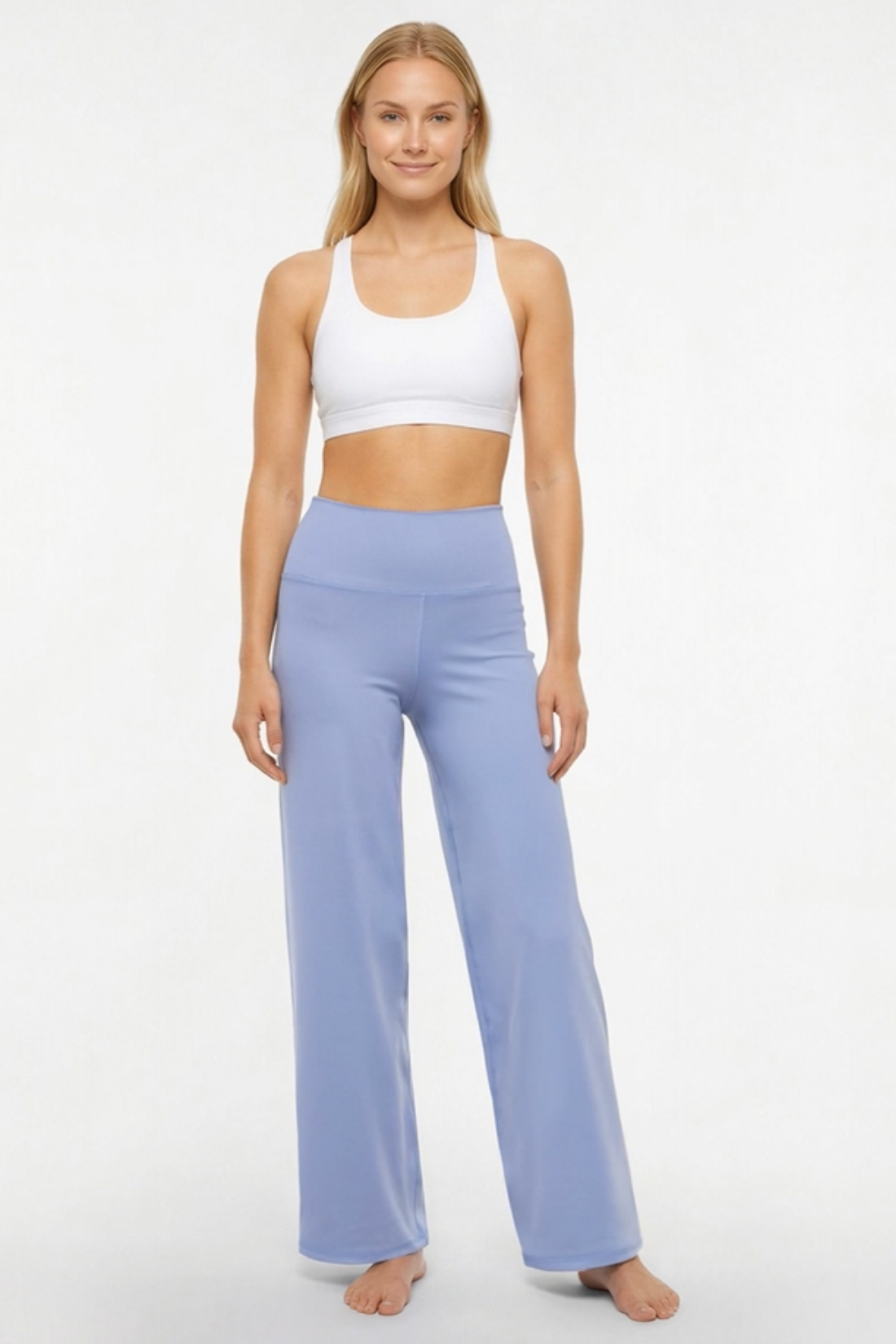 A woman modeling a two-piece activewear set consisting of a white sports bra and light periwinkle blue high-waisted wide-leg yoga pants, standing against a plain white studio background.