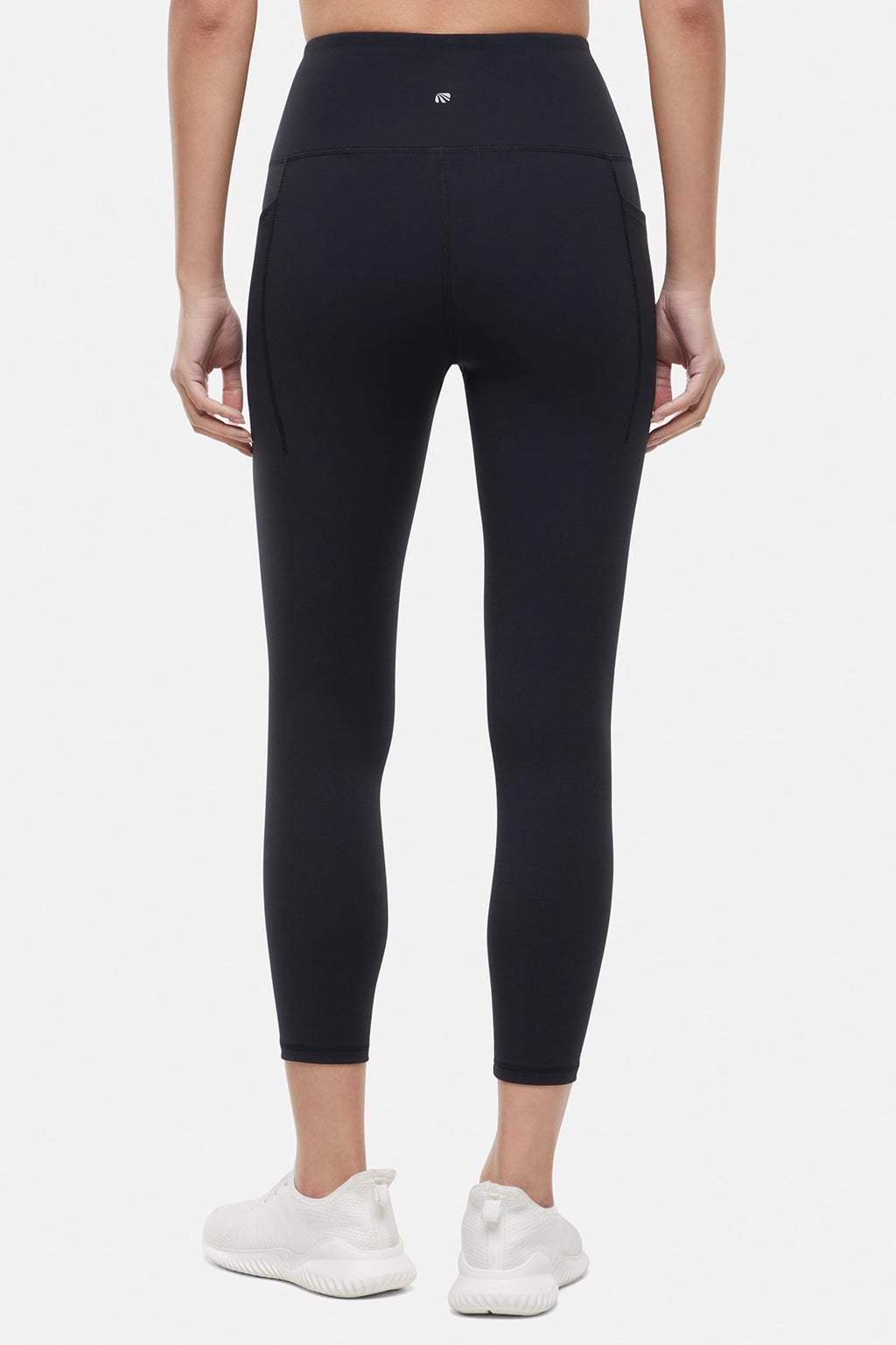 Back view of woman wearing black leggings worn by a person on a white background. #color_black