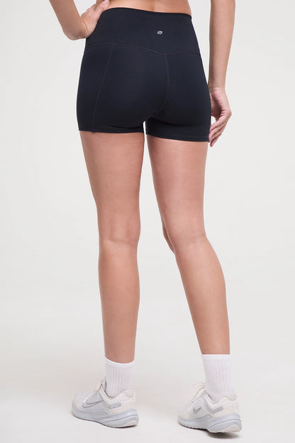 Back view of woman wearing black athletic shorts and white sneakers on a light background. 
