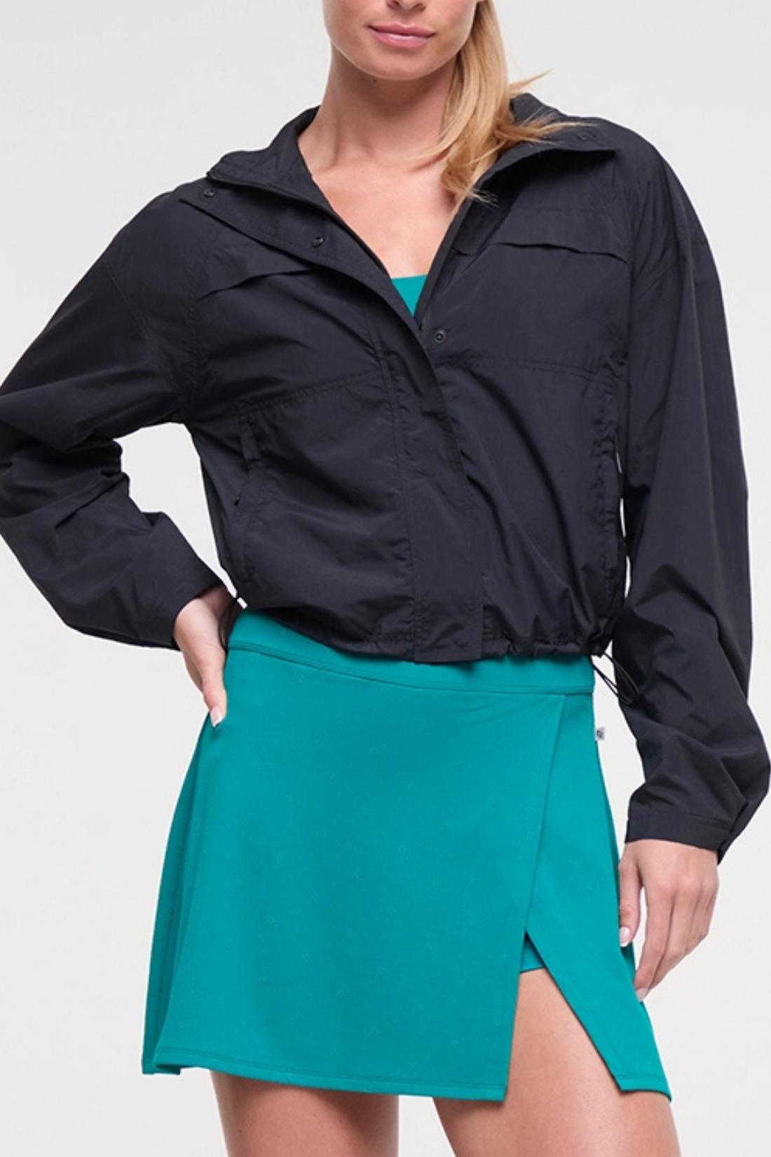 Front view of woman wearing a black jacket and teal skirt on a white background. 