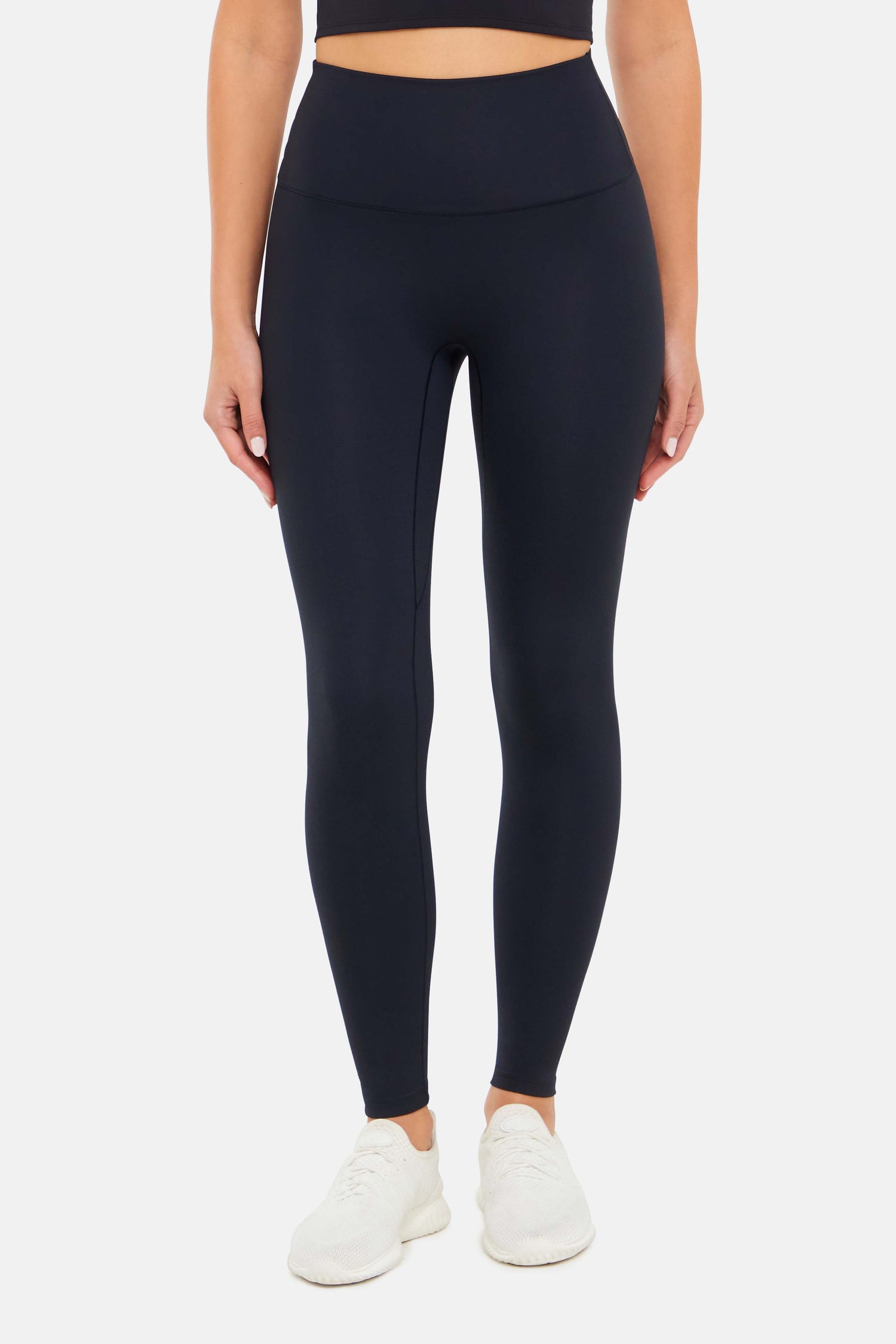 Front view of woman wearing black leggings on a white background. 