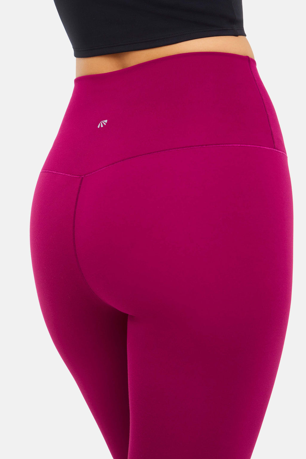 Close up back view of woman wearing bright burgundy leggings with small white logo on a white background. #color_magenta-purple