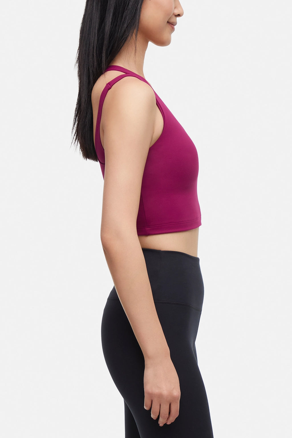 Side view of woman wearing a bright burgundy sports bra and black leggings on a white background. #color_magenta-purple