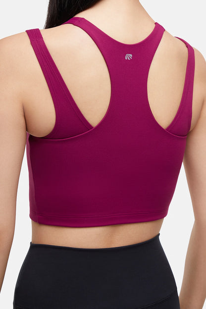 Close up back view of woman wearing a bright burgundy sports bra and black leggings on a white background. 