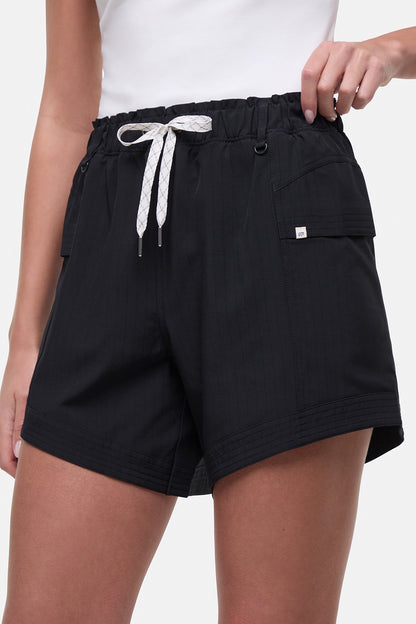 Close up side view of woman wearing black shorts with white drawstring waist and side pocket and white sneakers on a white background. 