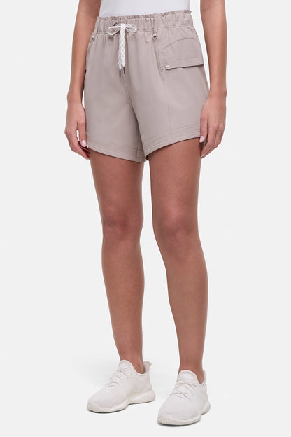 Front view of woman wearing beige  shorts with white drawstring waist and side pocket and white sneakers on a white background. 