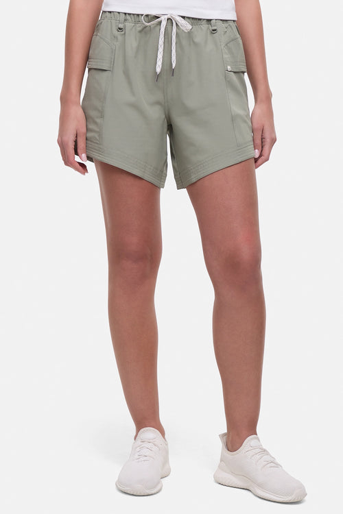 Front view of woman wearing sage green shorts with white drawstring waist and white sneakers on a white background. #color_shadow