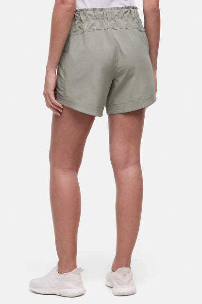 Back view of woman wearing sage green shorts and white sneakers on a white background. 