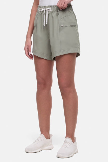 Side view of woman wearing sage green shorts with white drawstring waist and with side pockets and white sneakers on a white background. 