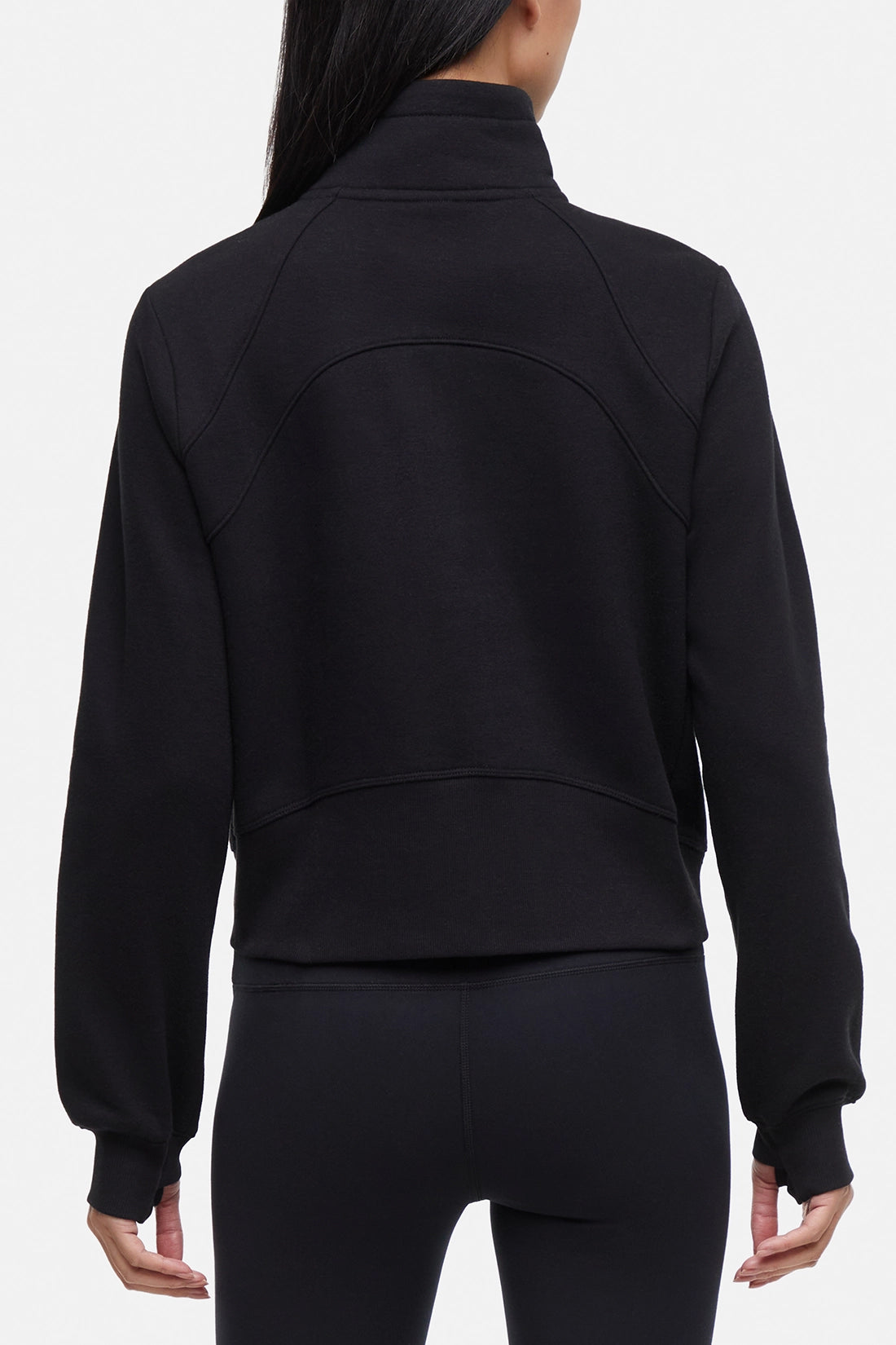Back view of woman wearing black half-zip pullover with thumbholes on a white background. 