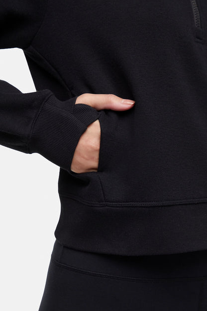 Front close up view of woman wearing black half-zip pullover with thumbholes on a white background. 