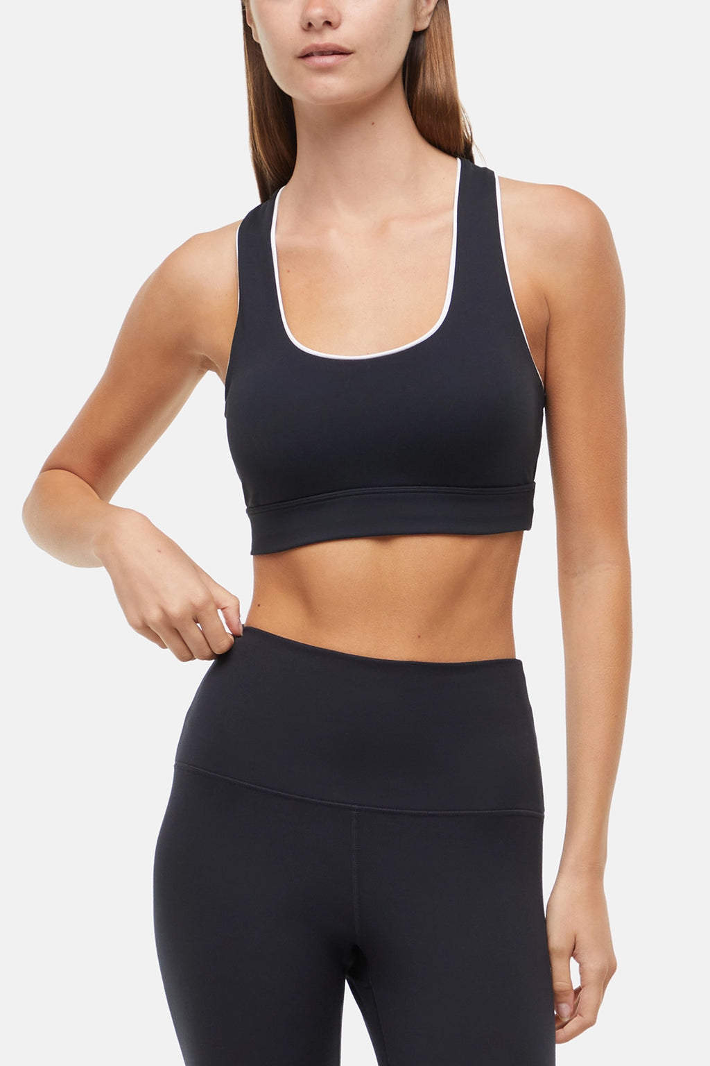 Front view of woman wearing a black sports bra with white trim and black leggings on a white background. #color_black