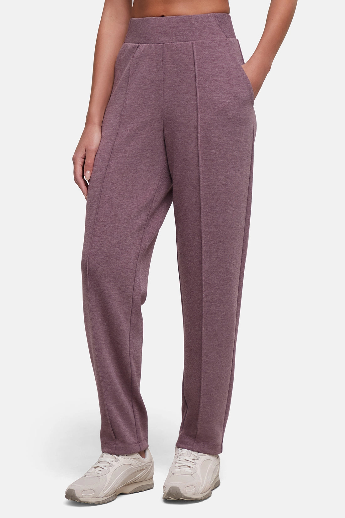 A person wearing heathered mauve-purple jogger-style pants with a wide waistband and side pockets, paired with white sneakers, against a light gray studio background. #color_heather-fig