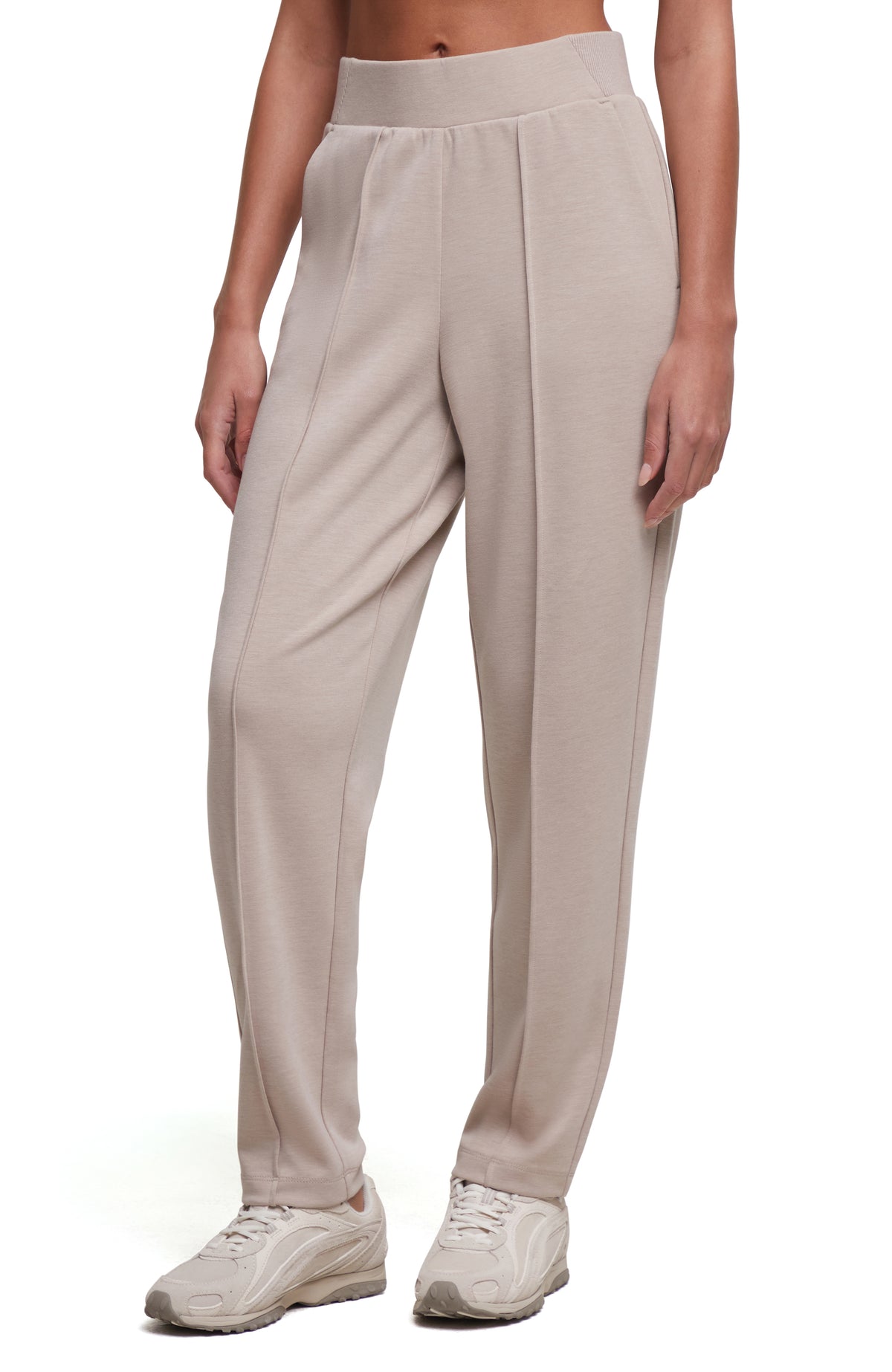 A model wearing light beige high-waisted athletic pants with a wide elastic waistband and relaxed straight legs, paired with white sneakers, against a plain white background. #color_heather-atmosphere