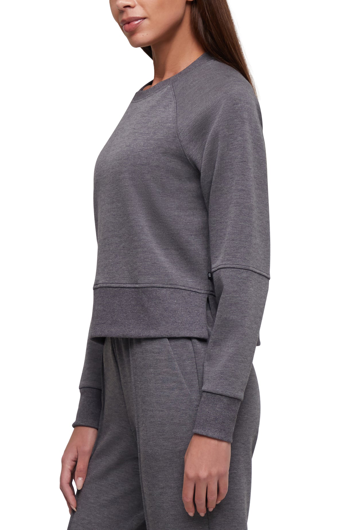 A woman wearing a heather gray long-sleeve cropped sweatshirt and matching jogger pants, shown in a side-profile studio shot against a white background. #color_heather-black