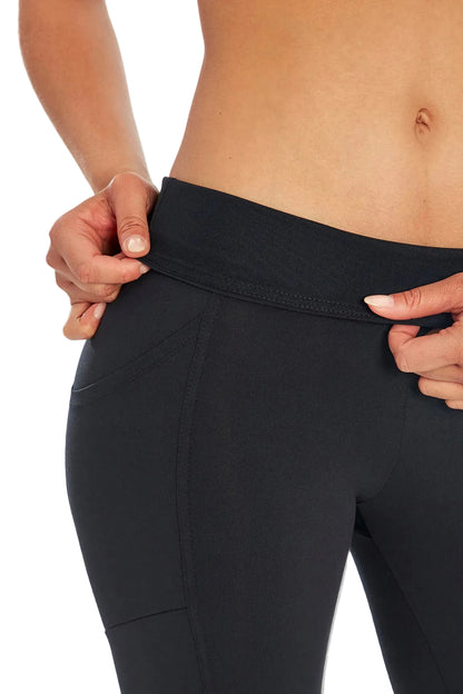 Close up front view of woman wearing black leggings folding over waistband on a white background. 