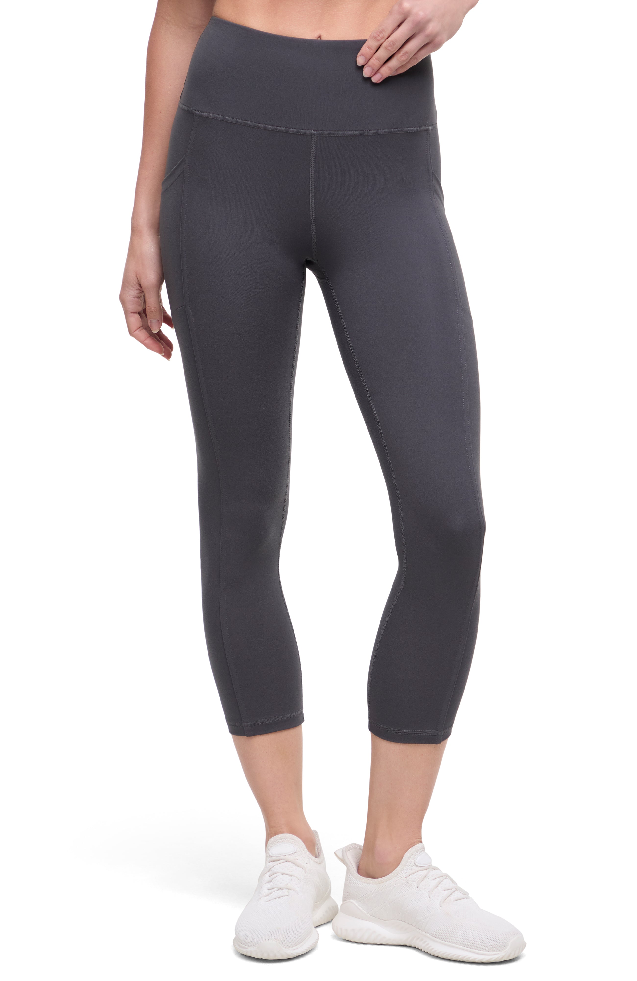 Front of woman wearing dark gray leggings with a white background. 