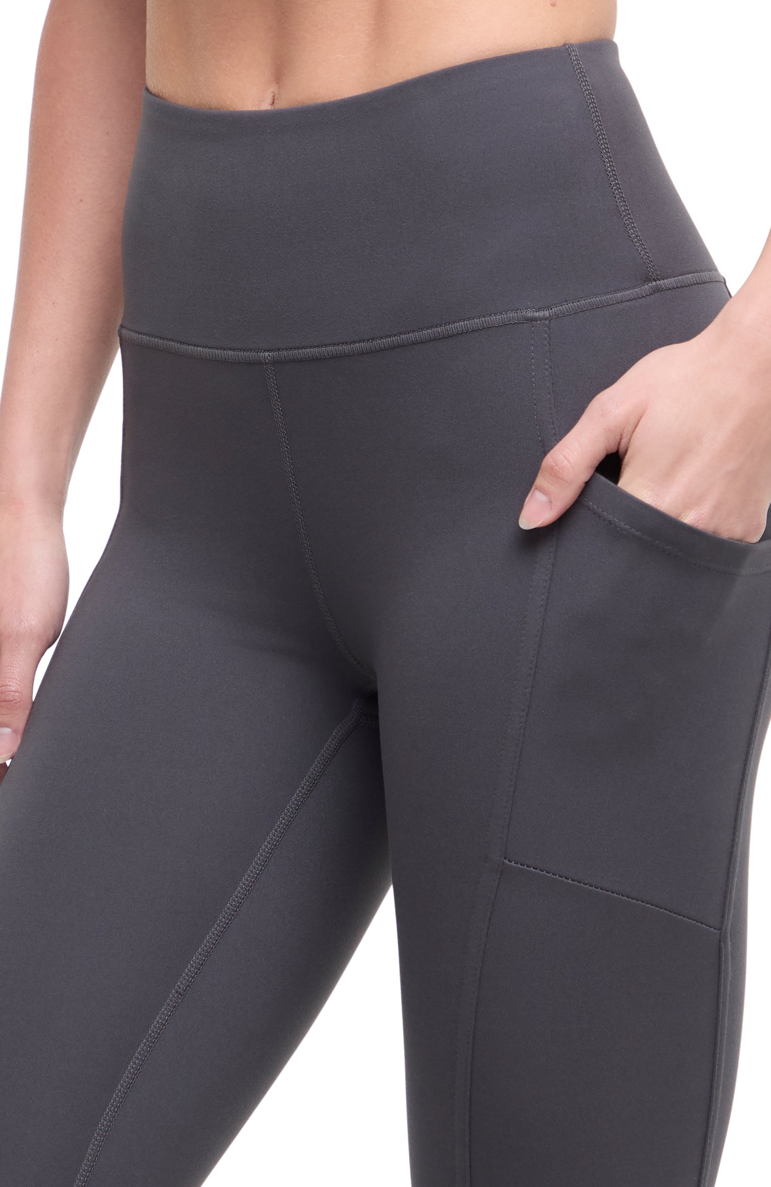 Close up front of woman wearing dark gray leggings with hand in pocket on a white background. 