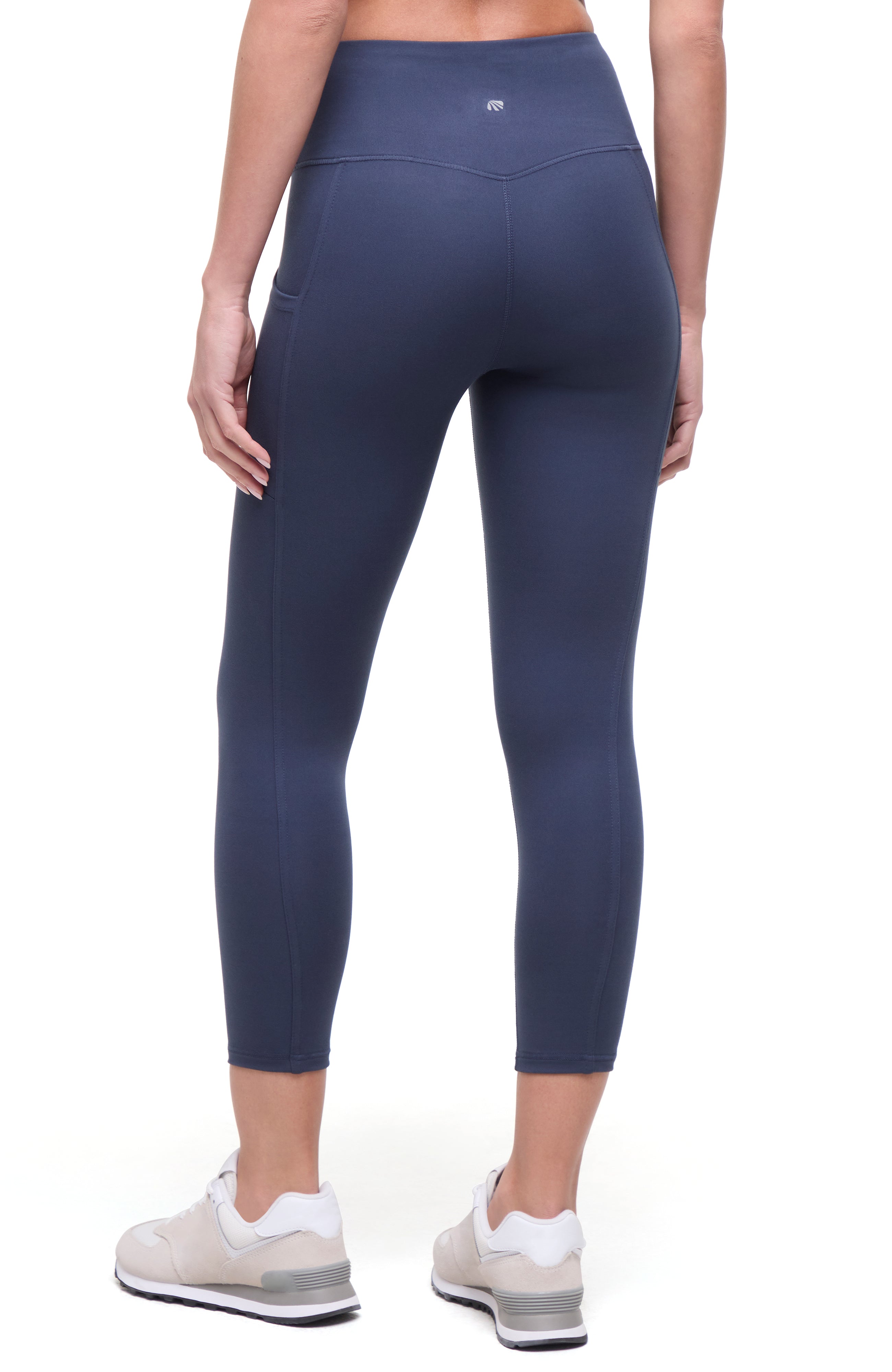 Back view of woman wearing navy blue leggings on a white background. 