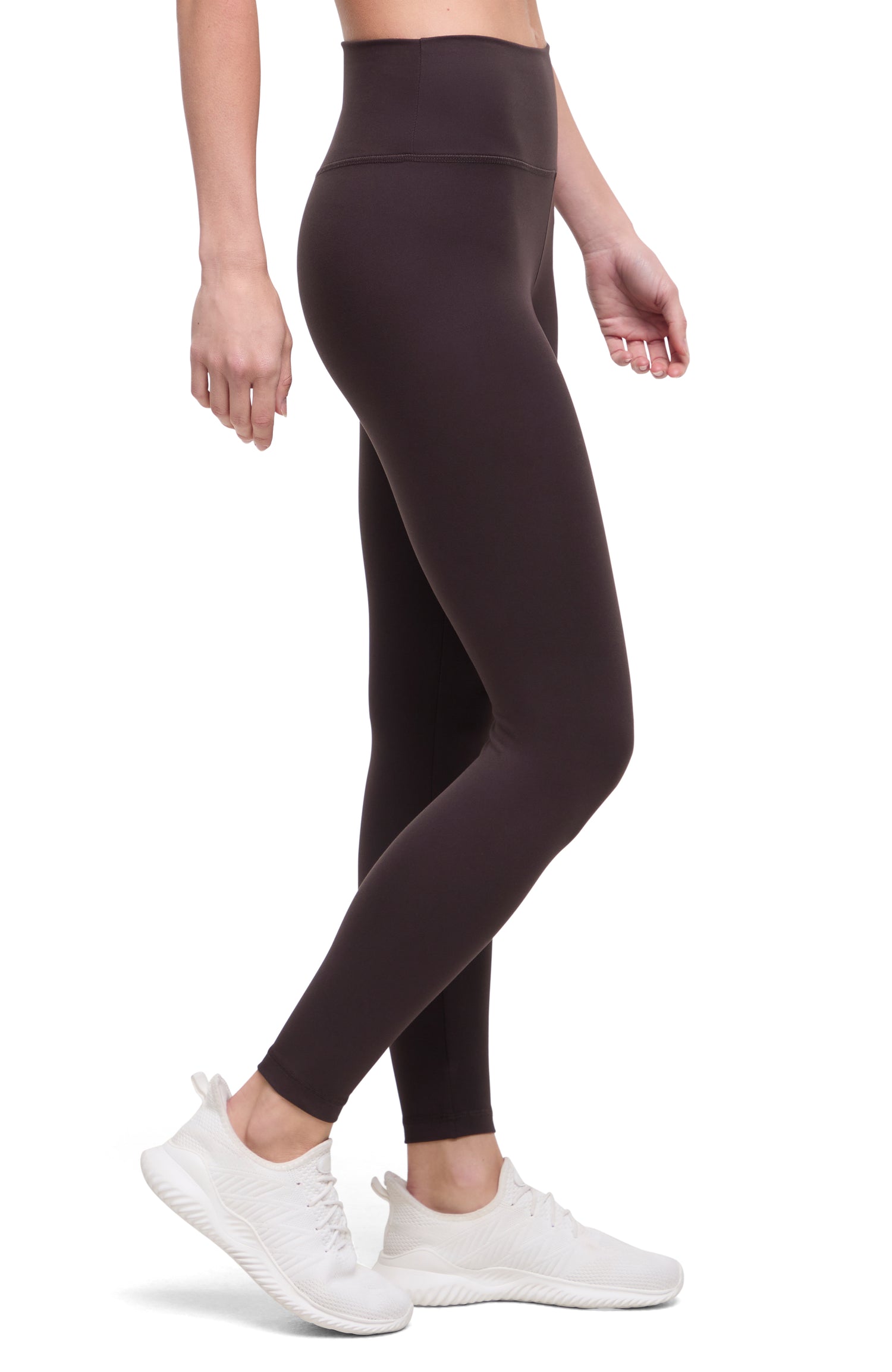 Side view of woman wearing dark brown leggings with a white background. 