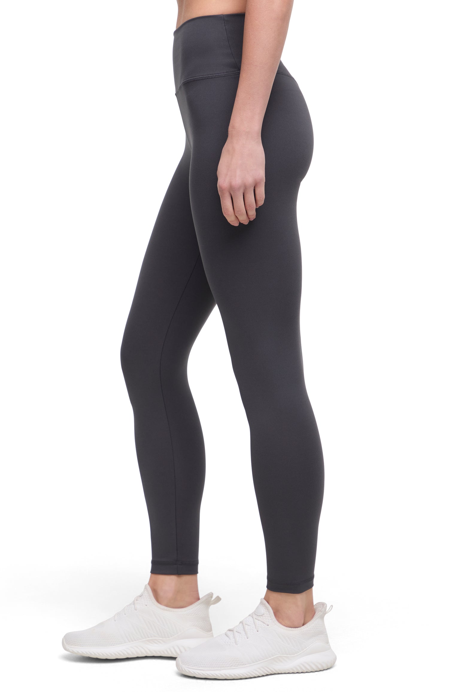 Side view of woman wearing dark gray leggings with a white background. 