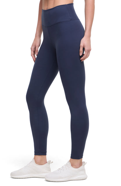 Side view of woman wearing navy leggings with a white background. 