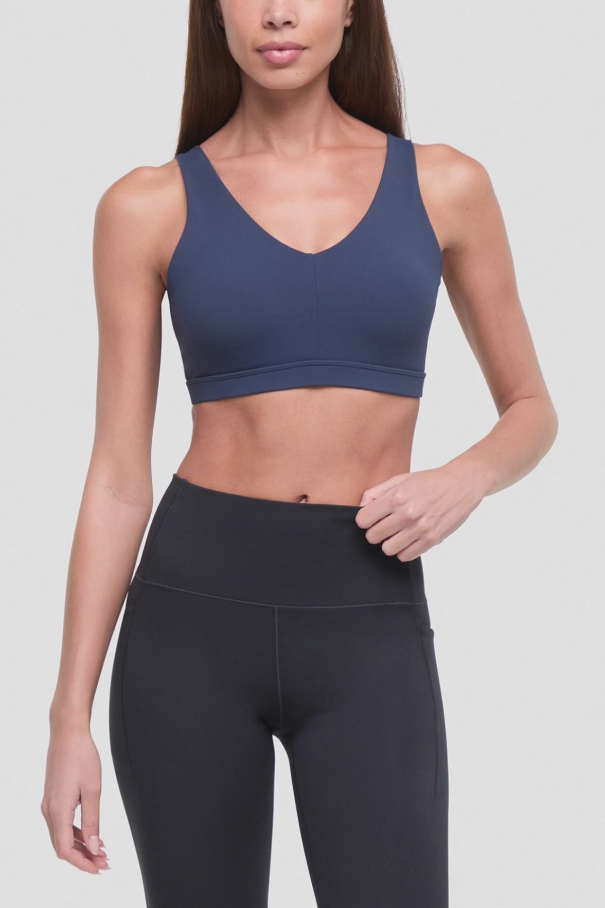 Video of a woman modeling a navy blue sports bra with cutout back straps and black high-waisted leggings against a light gray studio background. #color_total-eclipse
