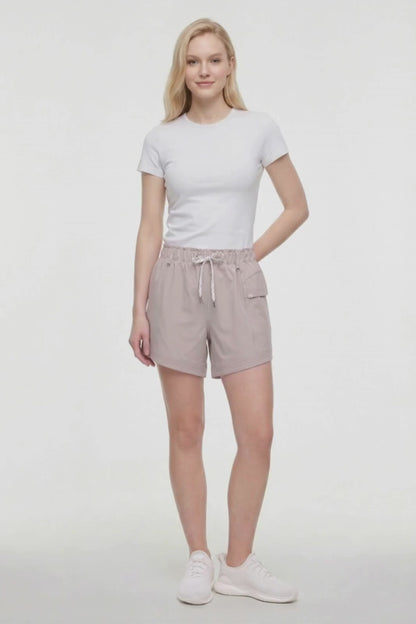 Video view of woman wearing beige shorts with white drawstring waist and side pocket and white sneakers on a white background. 