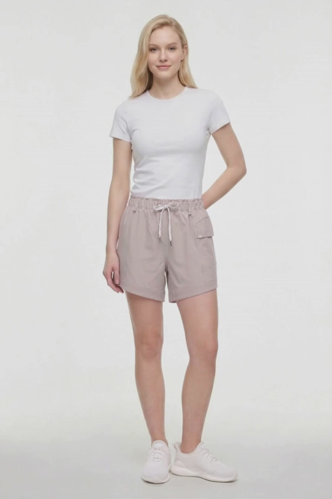 Video view of woman wearing beige shorts with white drawstring waist and side pocket and white sneakers on a white background. #color_atmosphere