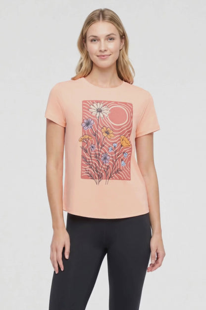 Video view of woman wearing a peach t-shirt with floral graphic on a light gray background. 