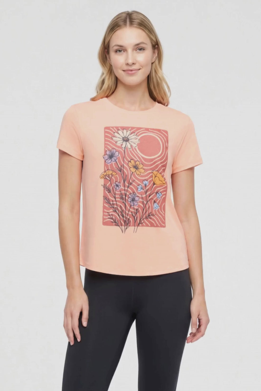 Video view of woman wearing a peach t-shirt with floral graphic on a light gray background. #color_heather-melon-ice-daisies-in-the-sun