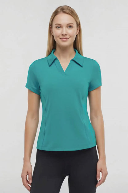 Video view of woman wearing a teal polo shirt and black pants on a white background. 