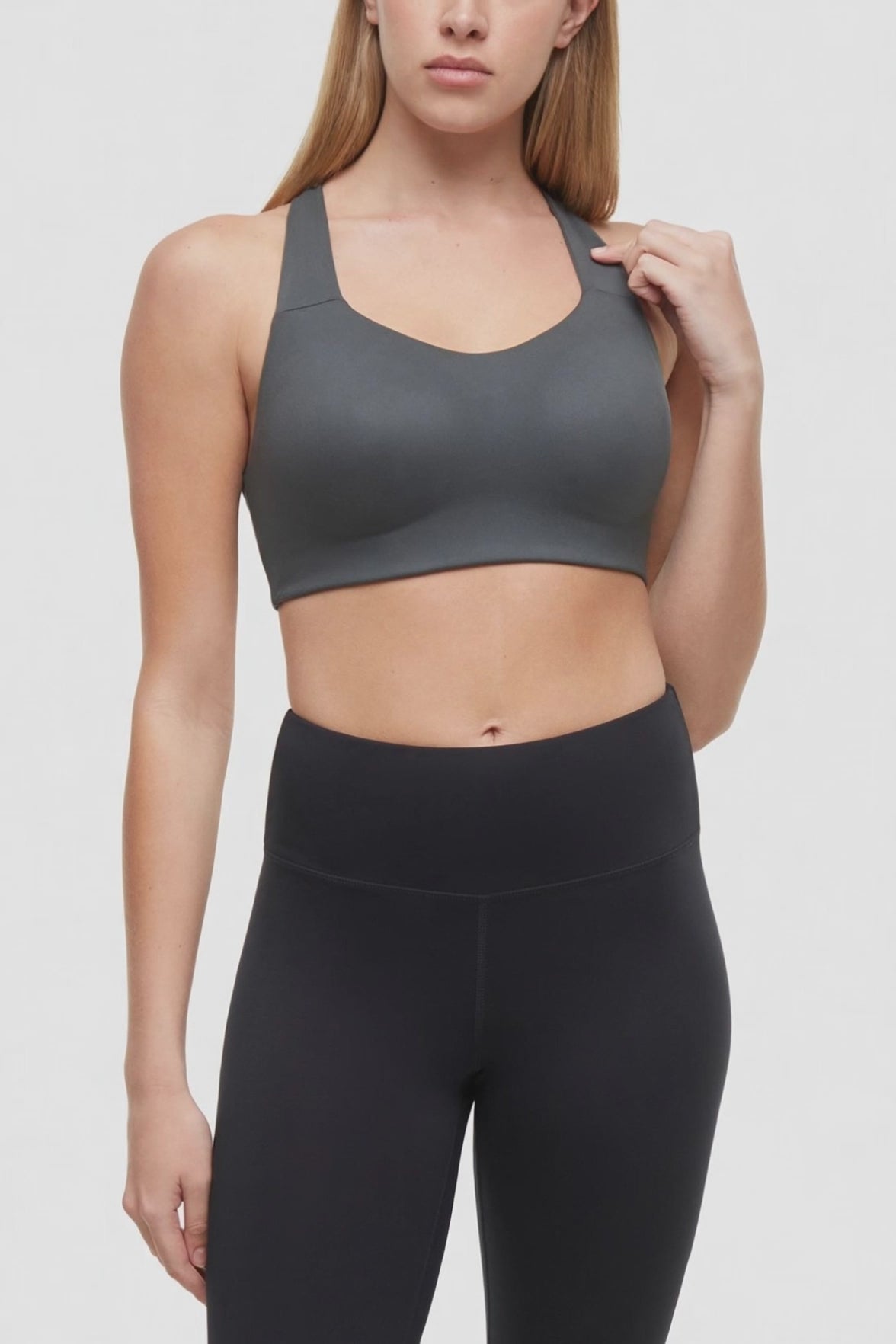 Video view of woman wearing a gray sports bra with strappy back and black leggings on a white background. #color_urban-chic