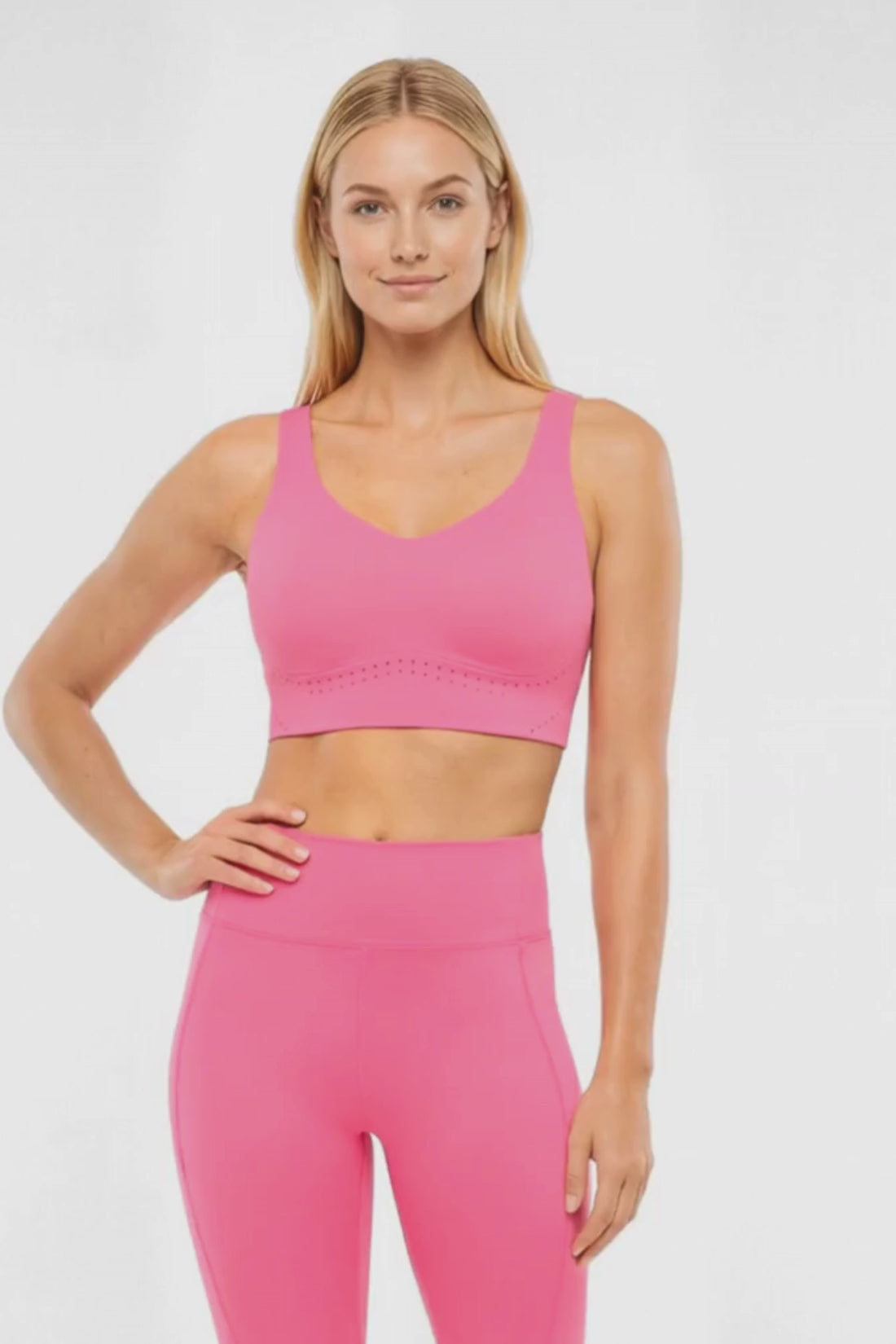 Video view of woman wearing a pink sports bra and matching pink leggings on a white background.  