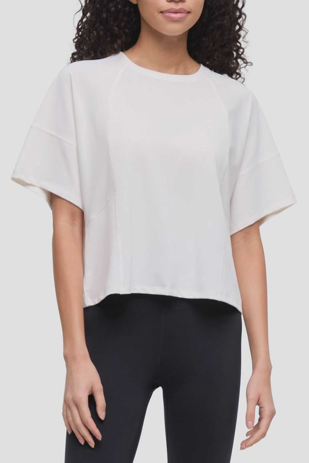 Video of a woman wearing a white short-sleeve crop top with wide sleeves and black leggings, shown from the shoulders to the upper thighs against a plain light background.  #color_sugar-swizzle